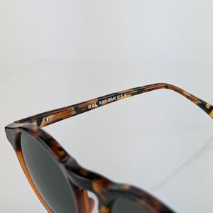 May include: Tortoiseshell sunglasses with dark lenses. The frame features a classic design with a brown and black pattern. The text "B&L RAY-BAN U.S.A." is printed on the temple.
