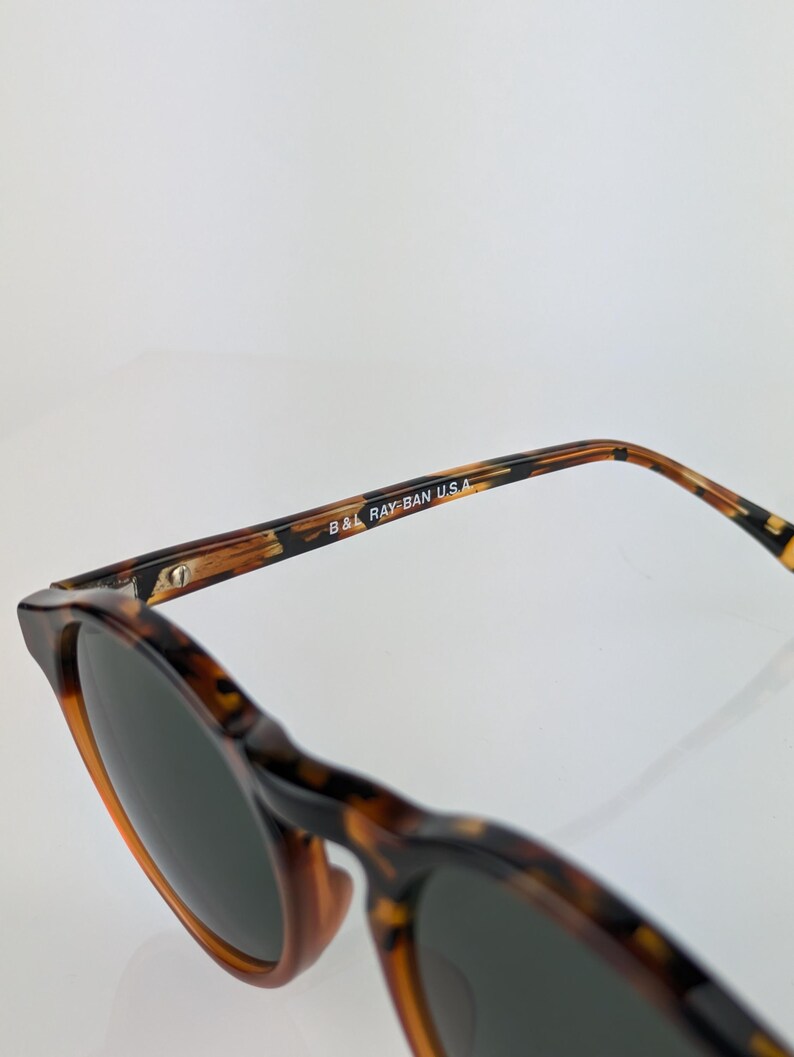 May include: Tortoiseshell sunglasses with dark lenses. The frame features a classic design with a brown and black pattern. The text "B&L RAY-BAN U.S.A." is printed on the temple.