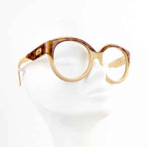 May include: Vintage eyeglasses with a tortoiseshell and beige frame. The round frames have a gold accent on the temples. The glasses are displayed on a white mannequin head.