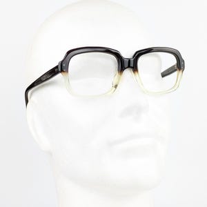 May include: Eyeglasses featuring a thick, rectangular frame with a dark brown upper section that transitions into a translucent, clear lower section. The temples are dark brown, and the clear lenses are set within the two-tone plastic frame.