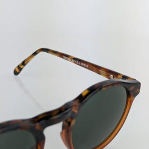 May include: Close-up of Gatsby style sunglasses with a tortoise shell pattern. The sunglasses have dark lenses and the text "Gatsby Style 1 W1516" is printed on the arm.