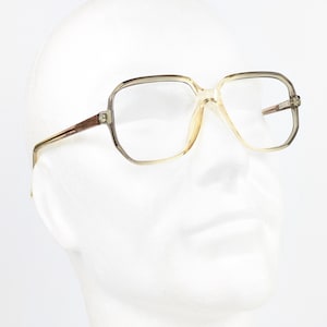 May include: Clear, translucent beige-tinted eyeglasses with a rectangular frame shape. The glasses feature thin, light-colored temples and a bridge that connects the two lenses. The frame has a subtle gradient effect, appearing darker at the top.