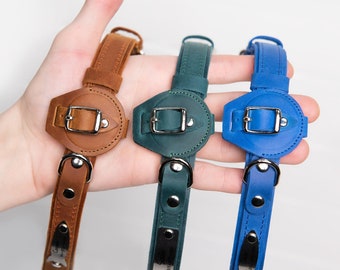 May include: Three leather dog collars in brown, green, and blue. Each collar has a metal buckle and a round metal tag.