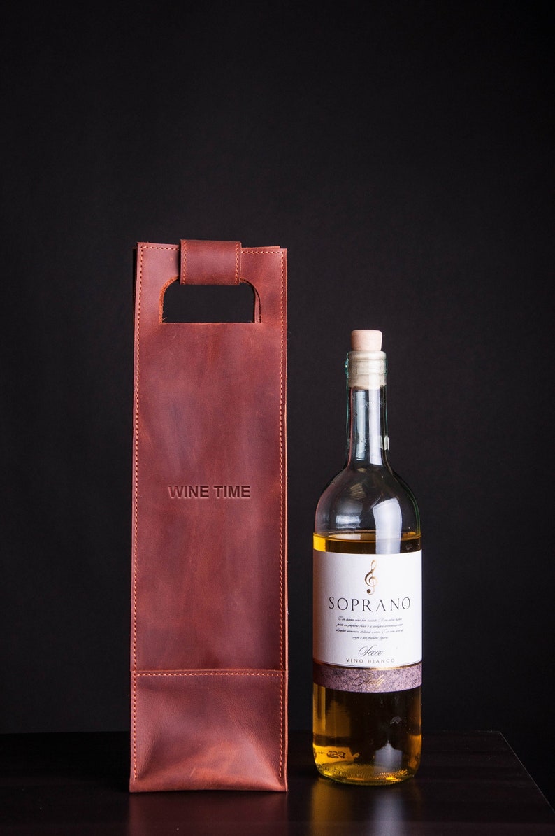 Personalized leather wine bottle carrier engraved "Wine Time" in rich brown leather, romantic anniversary wine gift for him displayed beside white wine bottle on dark background