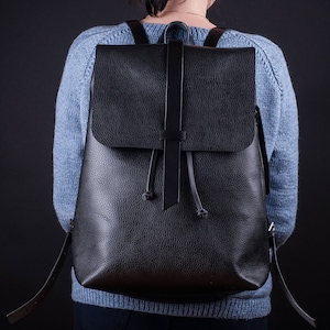 May include: A black leather backpack with a flap closure and adjustable straps.