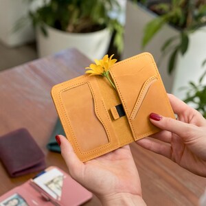 May include: A yellow leather wallet with a yellow flower tucked inside. The wallet has two pockets and a slot for cards.