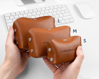 May include: Three brown leather cord organizers in different sizes, labeled "L", "M", and "S". The smallest organizer has the word "CORDZILLA" embossed on it.