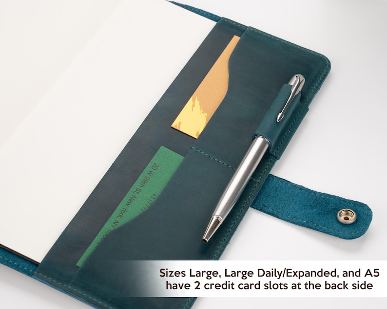 Pode incluir: Um di&aacute;rio de couro verde-azulado com uma caneta, um cart&atilde;o dourado e um cart&atilde;o verde nos bolsos. O di&aacute;rio est&aacute; aberto, revelando p&aacute;ginas brancas em branco. O texto na imagem diz: "Sizes Large, Large Daily/Expanded, and A5 have 2 credit card slots at the back side."