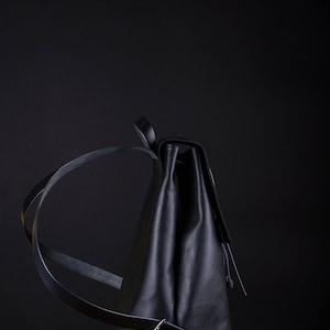 May include: A black leather backpack with a buckle closure and a drawstring top. The backpack is sitting on a green box.