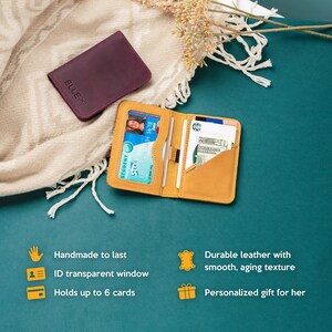 May include: A yellow leather wallet with a transparent window for an ID card. The wallet is open and has several cards inside. The wallet is on a teal surface with a white blanket and a small purple leather wallet in the background.