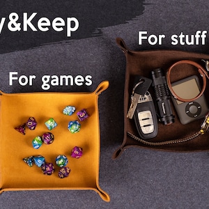 May include: Two leather trays, one brown and one yellow, with the text "Play & Keep" above. The brown tray contains a flashlight, keys, a watch, a music player, and a brown leather bracelet. The yellow tray contains a collection of colorful dice. The text "For games" is above the yellow tray and "For stuff" is above the brown tray.