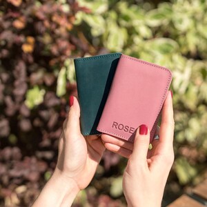May include: Two leather wallets, one green and one pink. The pink wallet has the word "ROSE" embossed on the front.