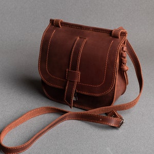 May include: A brown leather crossbody bag with a flap closure and a long adjustable strap.