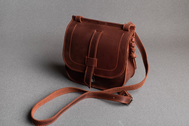 May include: A brown leather crossbody bag with a flap closure and a long adjustable strap.