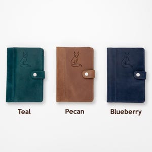 Pode incluir: Tr&ecirc;s cadernos de couro nas cores teal, pecan e blueberry. Cada caderno apresenta uma ilustra&ccedil;&atilde;o de raposa em relevo e um fecho de press&atilde;o. Os cadernos s&atilde;o exibidos em um fundo branco, com as cores rotuladas abaixo.