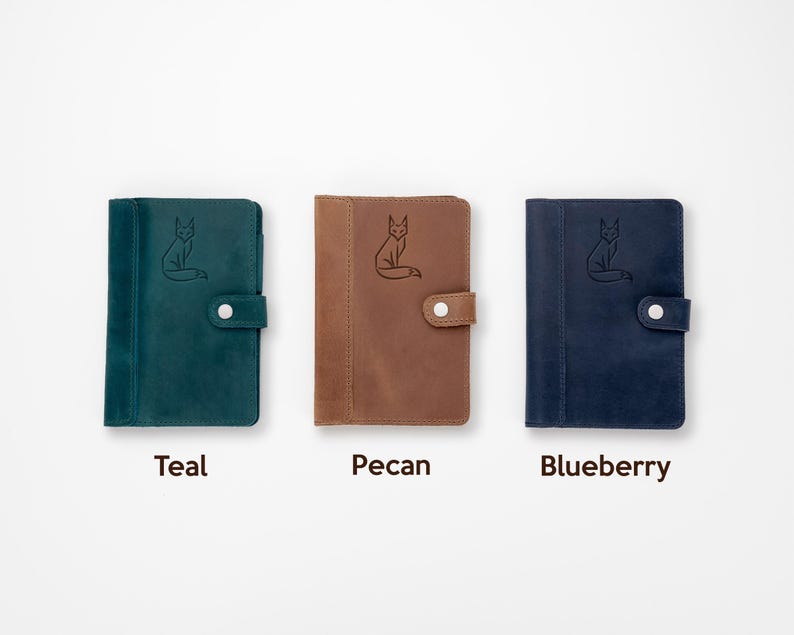 Pode incluir: Tr&ecirc;s cadernos de couro nas cores teal, pecan e blueberry. Cada caderno apresenta uma ilustra&ccedil;&atilde;o de raposa em relevo e um fecho de press&atilde;o. Os cadernos s&atilde;o exibidos em um fundo branco, com as cores rotuladas abaixo.