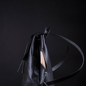 May include: A black leather backpack with a zippered pocket on the side. The backpack is sitting on a green surface.