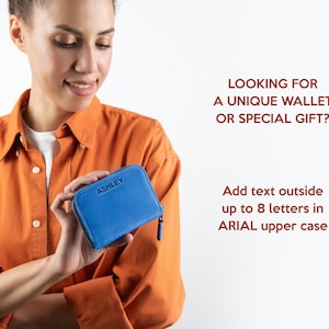 Op de afbeelding: Een klein blauw leren portemonnee met een ritssluiting. De portemonnee heeft de naam "ASHLEY" erop gegraveerd. De tekst "LOOKING FOR A UNIQUE WALLET OR SPECIAL GIFT? Add text outside up to 8 letters in ARIAL upper case" is zichtbaar op de achtergrond.