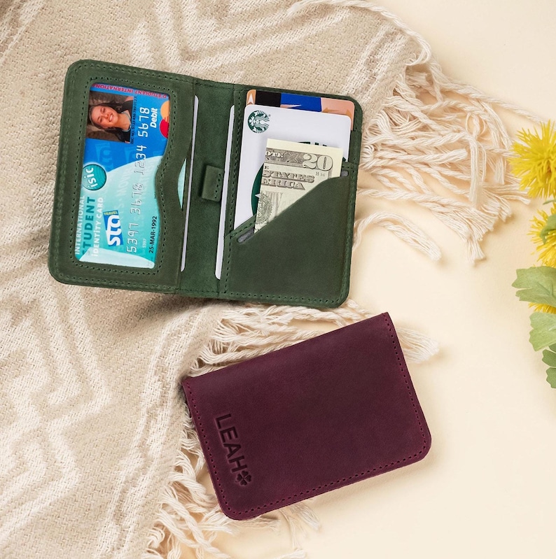 May include: Two leather wallets, one green and one burgundy. The green wallet has a card slot and a money pocket. The burgundy wallet has the name "LEAH" embossed on the front.