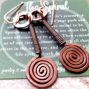 May include: Copper spiral earrings with a coiled design. The earrings hang from a copper hook and feature a spiral pendant. The earrings are displayed on a green card with the text "The Spiral".