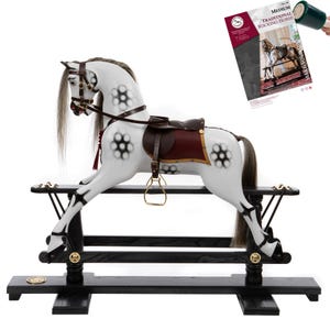 May include: A white dapple-grey rocking horse with a dark brown leather saddle, bridle, and stirrups, mounted on a black wooden base. The horse features a long grey mane and tail, and is accompanied by a brochure titled Medium Traditional Rocking Horse.