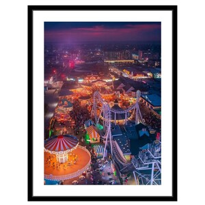 May include: An aerial view of a carnival at night. The carnival is lit up with colorful lights. There are rides, games, and food stalls. The Ferris wheel is in the foreground, and the roller coaster is in the background. The sky is a dark purple color, and the city lights are visible in the distance.