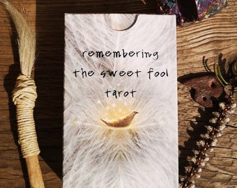 Può includere: Una carta bianca con il testo "remembering the sweet fool tarot" in scrittura nera. La carta presenta uno sfondo bianco e piumato con un uccello dorato al centro.