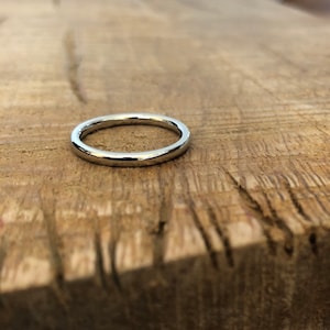 May include: A simple silver band ring, lying on a wooden surface.