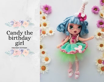 Puede incluir: Muñeca de crochet con cabello azul, un vestido rosa y verde y un sombrero blanco. La muñeca sostiene una flor rosa. La muñeca está rodeada de flores blancas.