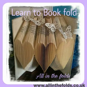 May include: A book folded into a heart shape with paper butterflies on top. The book is titled "Learn to Book fold" and the website "www.allinthefolds.co.uk" is displayed below the heart.