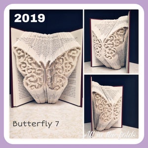 May include: A white book with a butterfly design folded into the pages. The book is open and the butterfly is visible. The book is titled "All in the folds" and the year "2019" is printed on the cover. The book is labeled "Butterfly 7".
