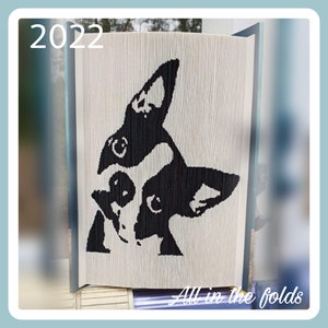Peut inclure: Une œuvre d'art de livre plié en noir et blanc représentant un Boston Terrier. Le livre est intitulé "All in the folds" et l'année "2022" est imprimée sur la couverture.