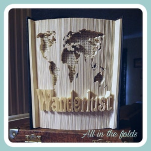 Peut inclure: Une sculpture d'art de livre représentant une carte du monde avec le mot "Wanderlust" plié dans les pages. Le livre est ouvert et debout sur une surface en bois.