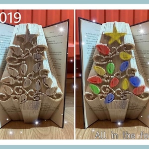 May include: A book folded into the shape of a Christmas tree with colourful lights and a star on top. The book is open and the pages are folded to create the shape of the tree. The text "All in the folds" is visible at the bottom of the image.