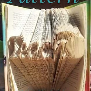 May include: A book folded into the shape of the word "Love" with the text "Mint the folds" at the bottom of the page. The book is open and the pages are folded to create the word.