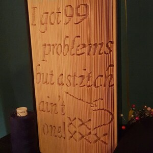 May include: A folded book art piece with the text "I got 99 problems but a stitch ain't one!" and "All in the folds" on the front cover. The book is made of paper and has a brown colour.