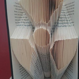 May include: A book folded into a 3D heart shape, with the text "Pattern only" at the top and "Allinthefolds" at the bottom. The book is sitting on top of another book.