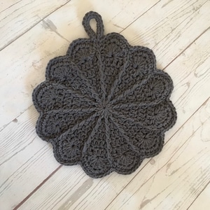 May include: Gray crocheted pot holder with a loop handle. The pot holder has a circular shape with a scalloped edge.