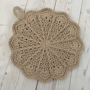 Peut inclure: Un dessous de plat en crochet beige avec une anse en boucle. Le dessous de plat est rond et a un bord festonné.
