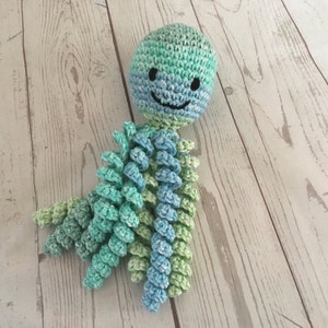 May include: A crocheted octopus toy with a smiling face. The octopus is made with blue and green yarn and has eight tentacles.