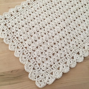 May include: A white crocheted doily with a scalloped edge. The doily is made with a delicate stitch pattern and has a soft, airy feel.