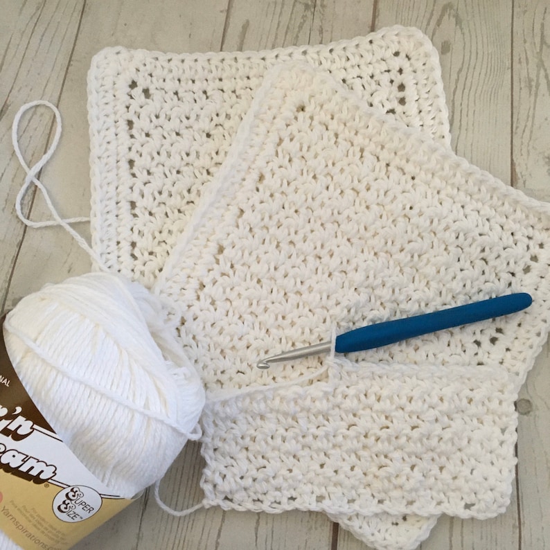 May include: A white crochet project in progress, featuring a ball of white yarn, a blue-handled crochet hook, and several completed sections of the project. The yarn is labeled "Sugar'n Cream" and is a super size.
