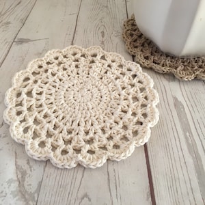 May include: A white crocheted coaster with a delicate, lacy design. The coaster is round and has a scalloped edge.