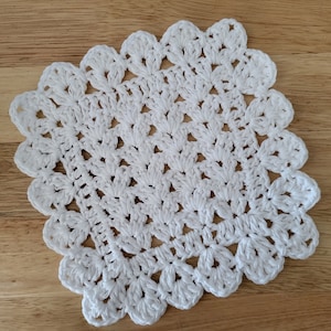 May include: White crocheted doily with a scalloped edge. The doily is made with a delicate stitch pattern and has a lacy appearance.