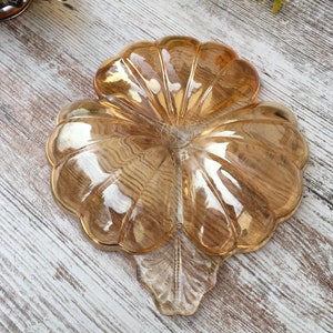 May include: A vintage amber-colored glass serving dish with a unique, scalloped petal design. The dish has a central circular area and a leaf-shaped base. The glass has a glossy finish, reflecting light and adding a touch of elegance to any table setting.