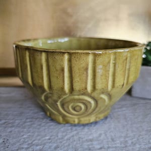Może przedstawiać: Ręcznie robiona, oliwkowozielona ceramiczna miska z pionowymi żebrowanymi detalami i spiralnym wzorem na dolnej części. Misa ma rustykalną, ziemistą estetykę.