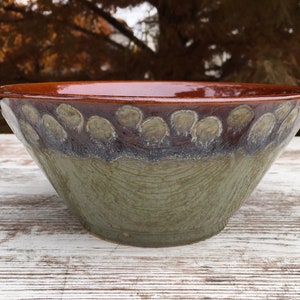 May include: A large, brown and green ceramic bowl with a decorative rim. The bowl has a speckled glaze and a slightly textured surface.