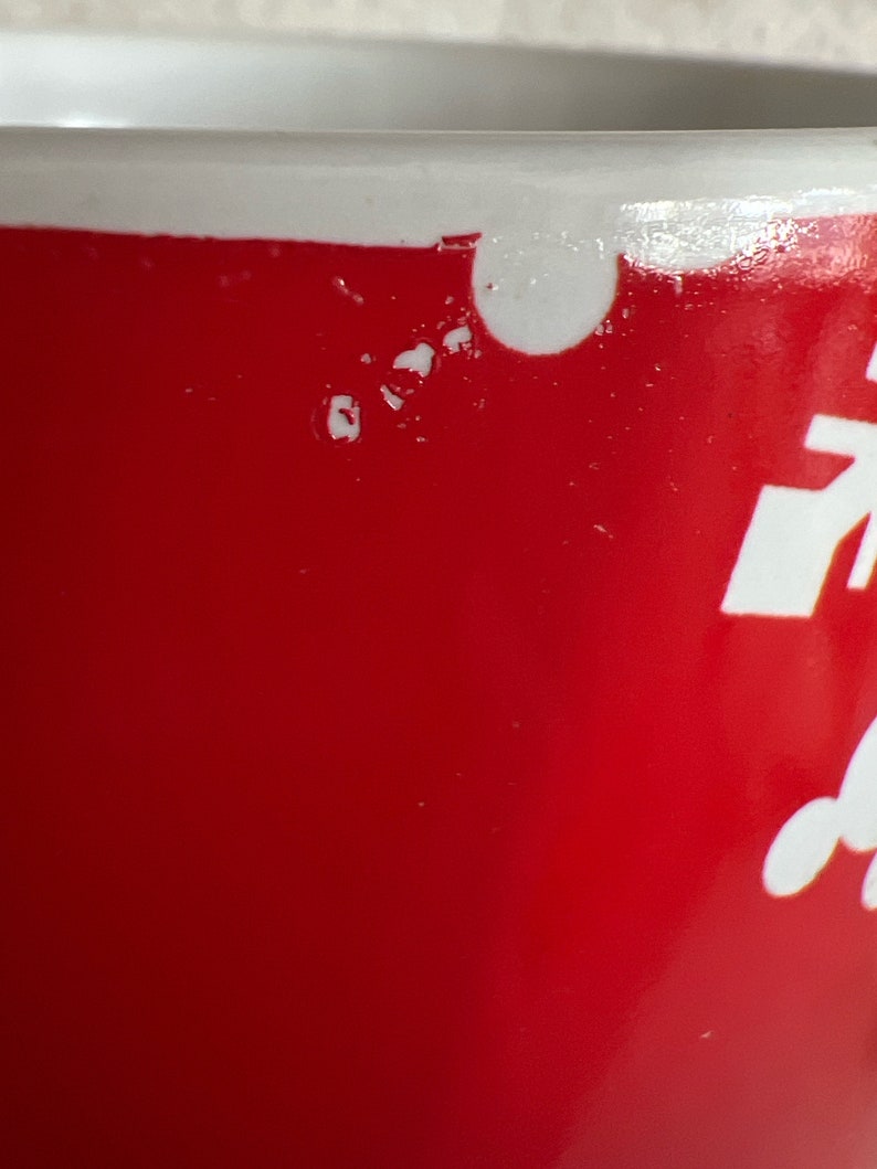 K&ouml;nnte beinhalten: Eine rote Keramiktasse mit wei&szlig;en Maldetails. Die Tasse hat einen Abplatzer am Rand.