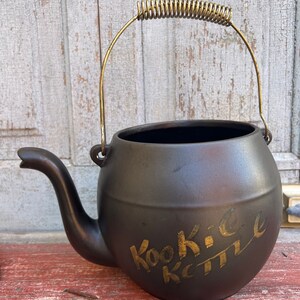 Puede incluir: Una taza de cerámica blanca con asa negra y el texto "But First, Coffee" en negrita negra. La taza se encuentra sobre un fondo borroso, sugiriendo un ambiente acogedor.