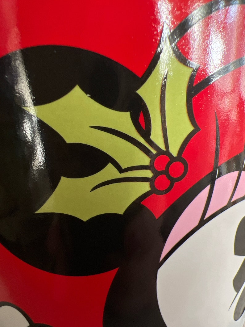 K&ouml;nnte beinhalten: Eine rote Tasse mit einer Schwarzwei&szlig;illustration einer Comicfigur, die einen gr&uuml;nen Stechpalmenzweig mit roten Beeren tr&auml;gt.